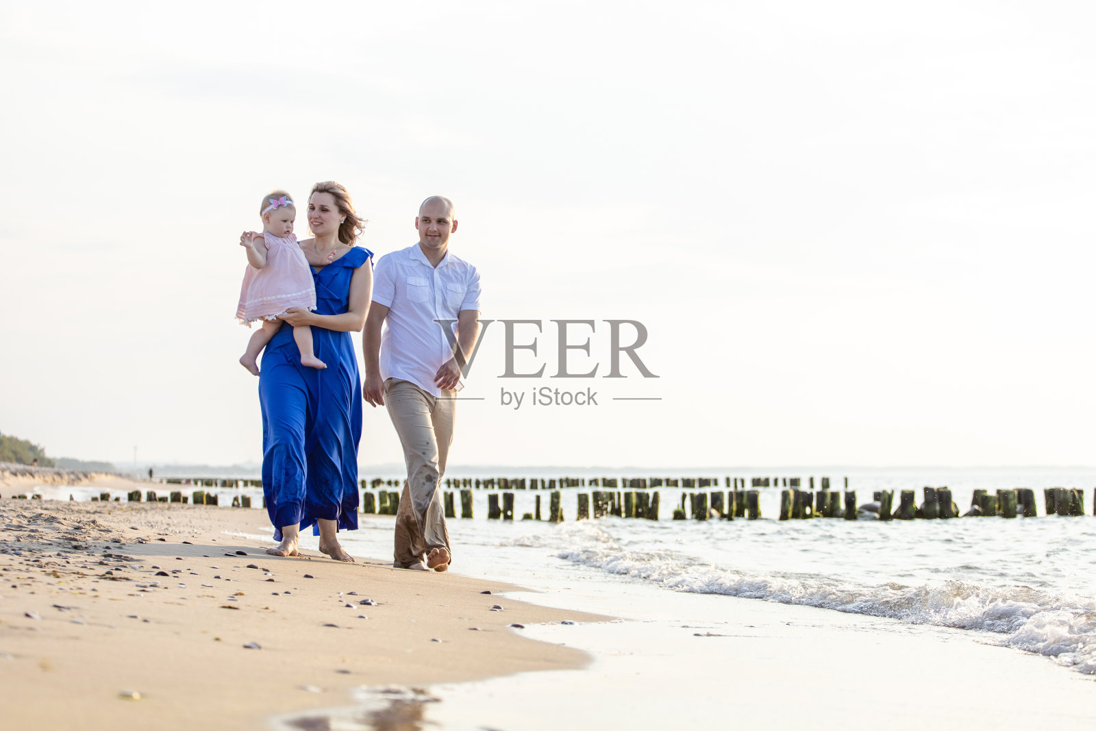 夏日的傍晚，一个年轻幸福的家庭带着一个小孩在海上散步照片摄影图片