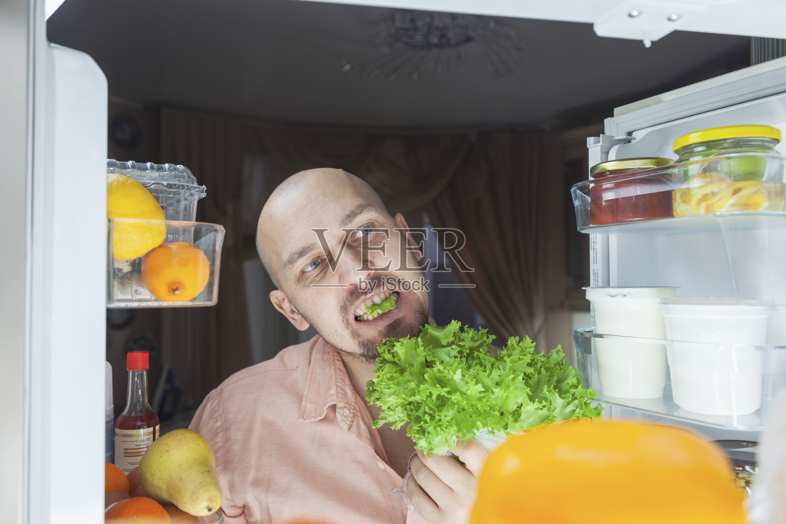 饥饿的人。一个男人在晚上看着冰箱，一个饥饿的男人一看就准备吃所有的东西，吃着莴苣照片摄影图片