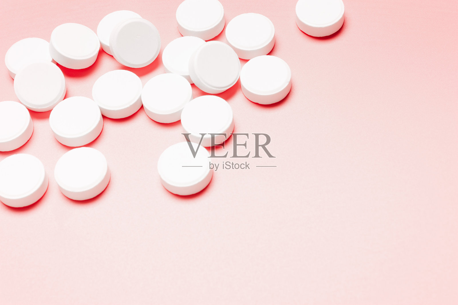 粉色背景下的白色圆形药丸。照片摄影图片