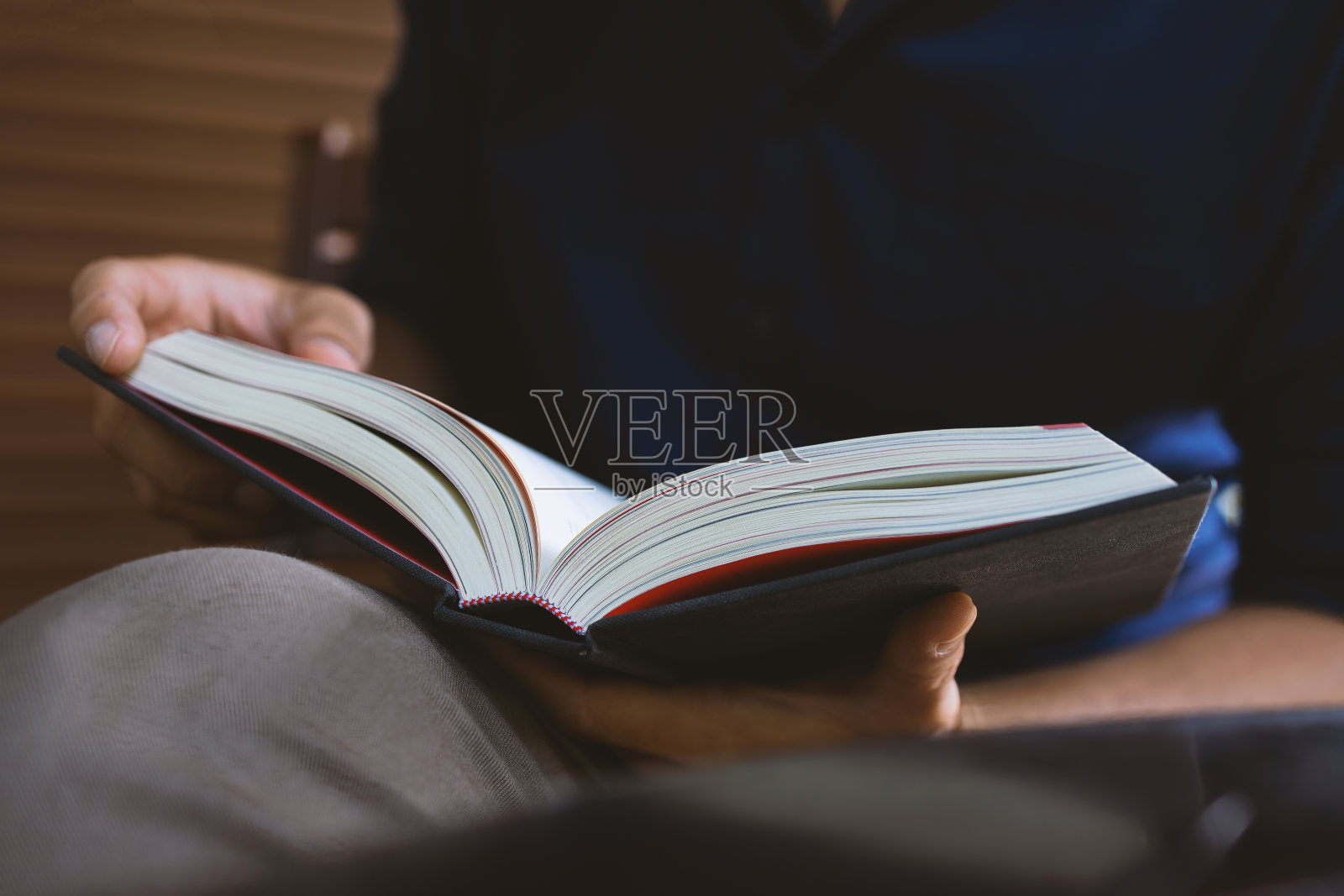 年轻人正坐在房间的窗户上看书，背景是柔焦和过光照片摄影图片