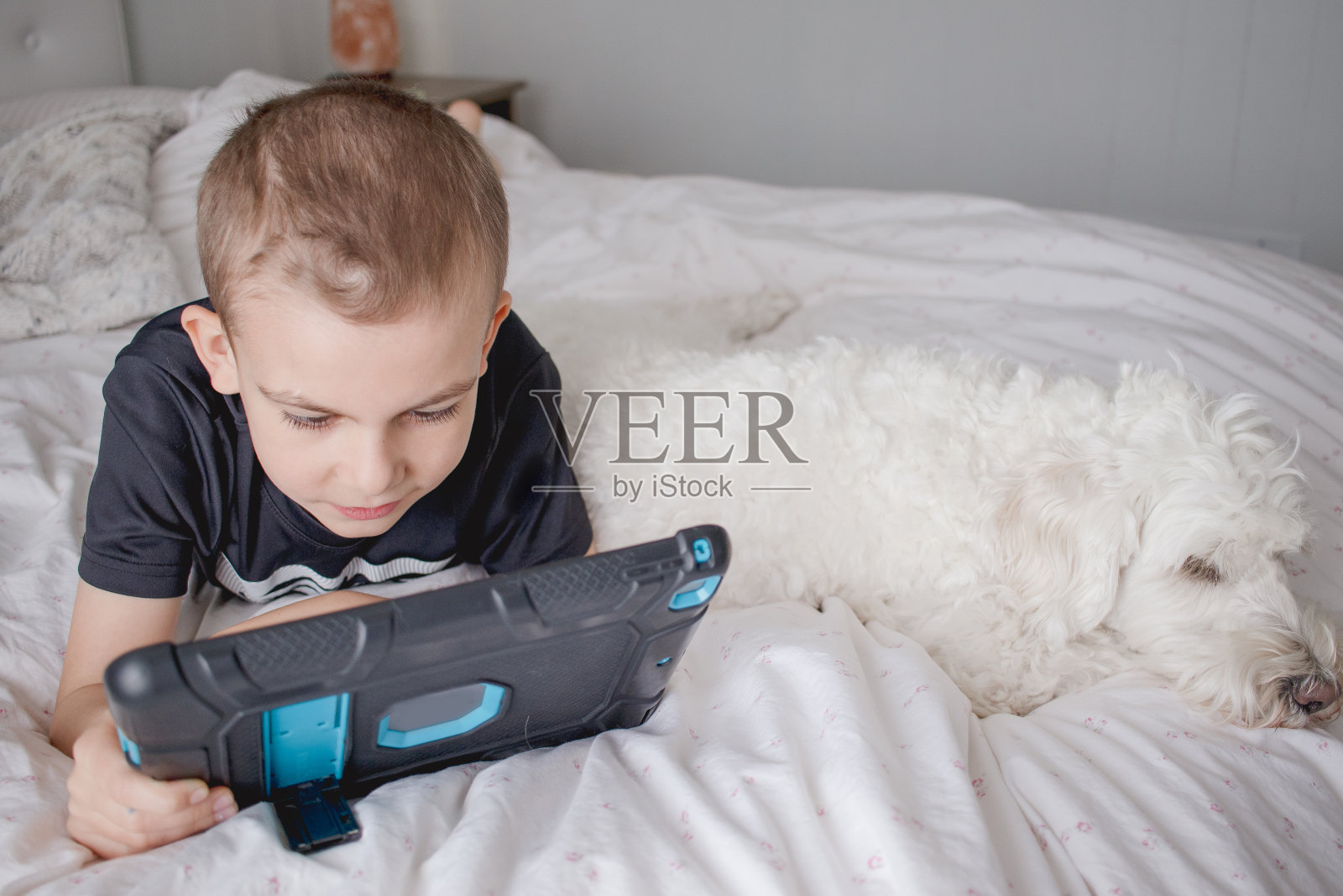 小男孩躺在床上用iPad说话照片摄影图片