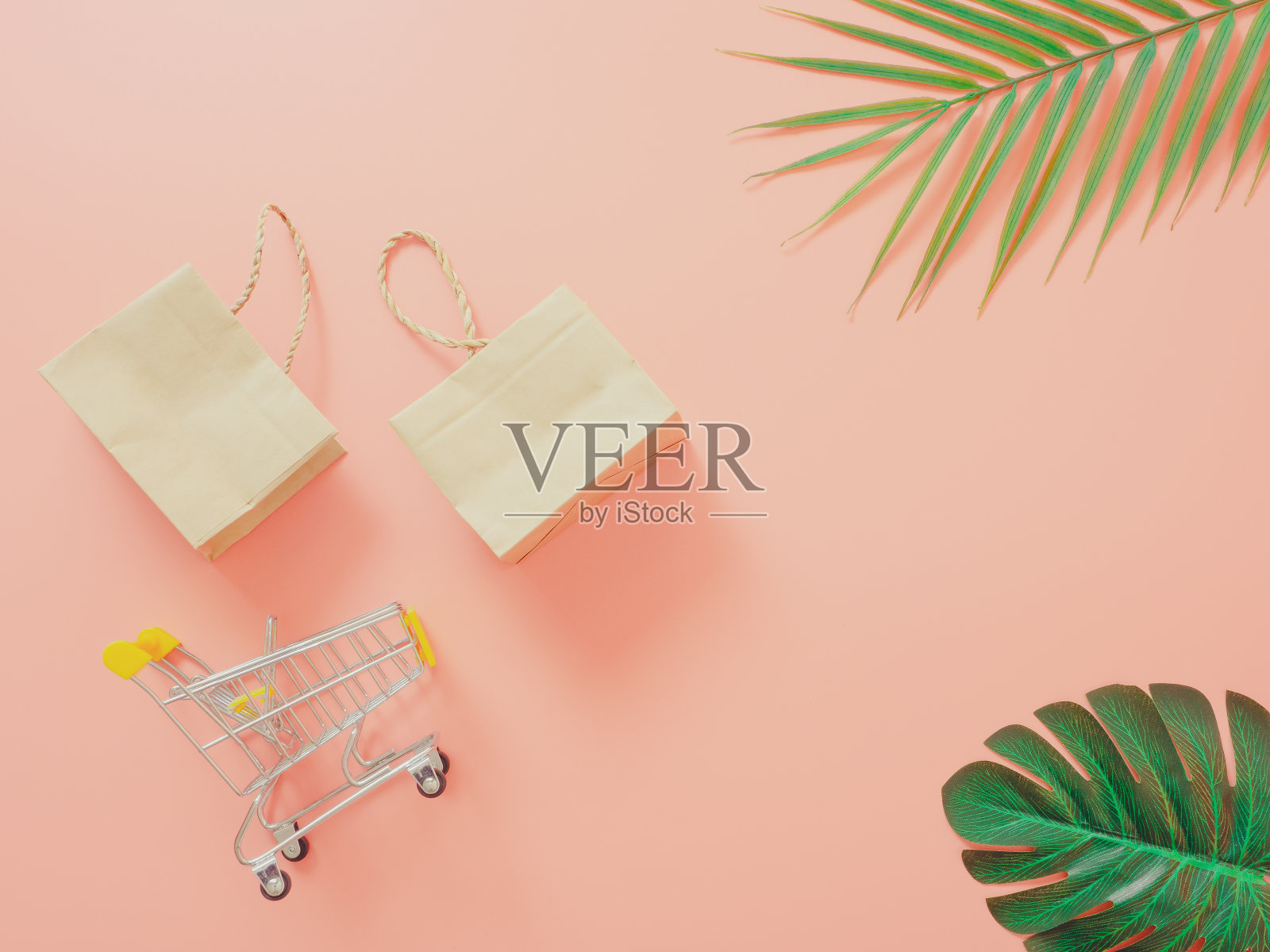 夏季购物概念从小手推车和纸购物袋在柔和的粉红色背景。前视图。照片摄影图片