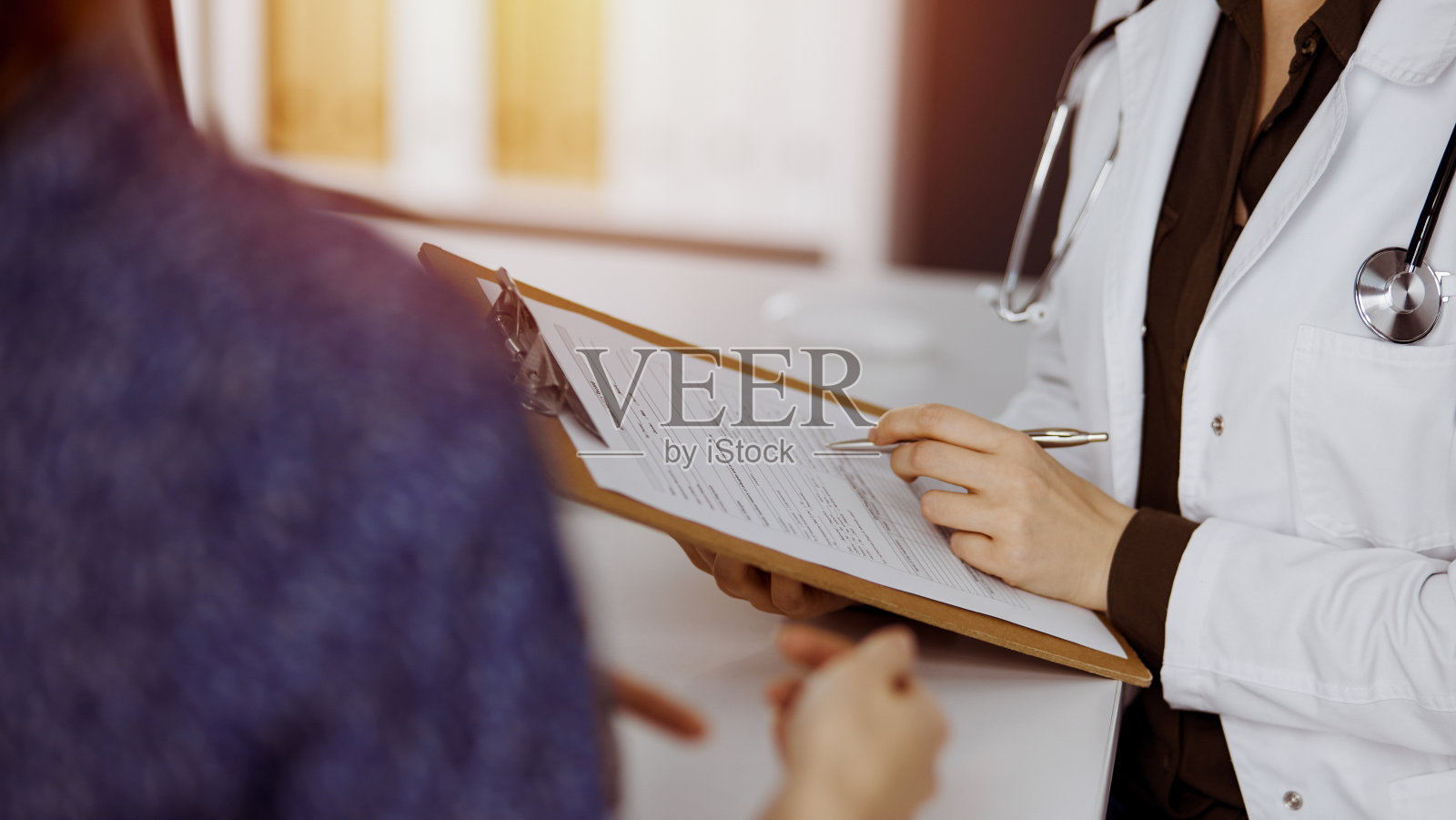 医生和病人坐在阳光诊所讨论当前的健康检查。医院完善的医疗服务照片摄影图片