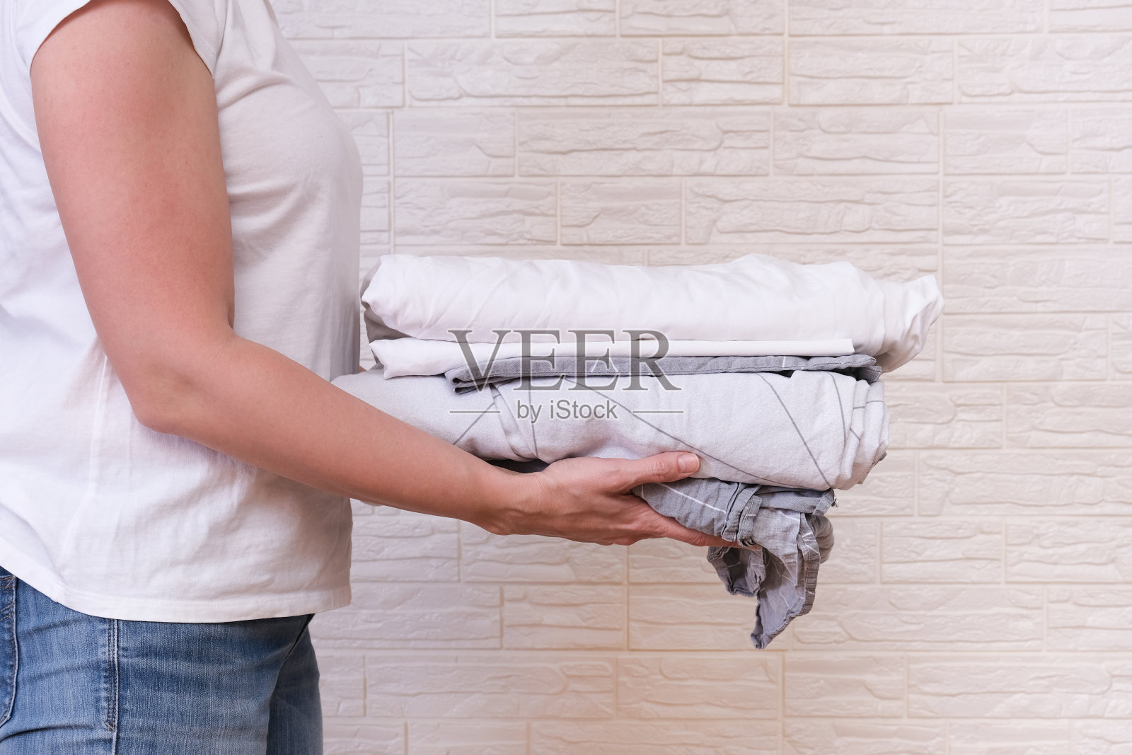 一个妇女家庭主妇拿着一堆洗过的叠好的床单。洗衣服和亚麻布，家居概念照片摄影图片