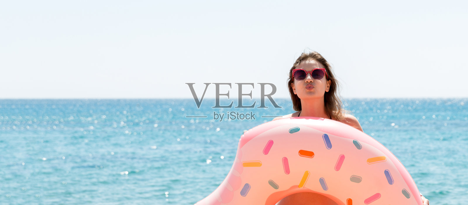 年轻女子拿着甜甜圈充气圈在海边亲吻照片摄影图片