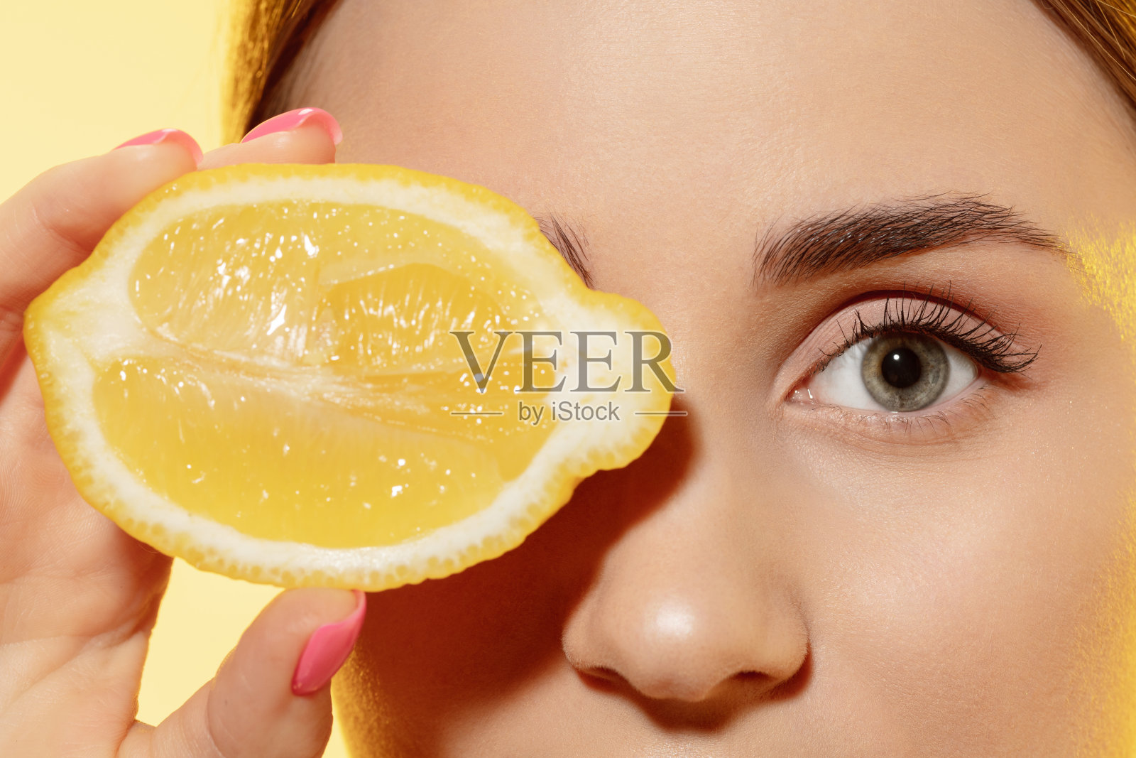 特写美丽的女性的脸与柠檬片在黄色的背景。化妆品、自然生态护理、皮肤护理。照片摄影图片