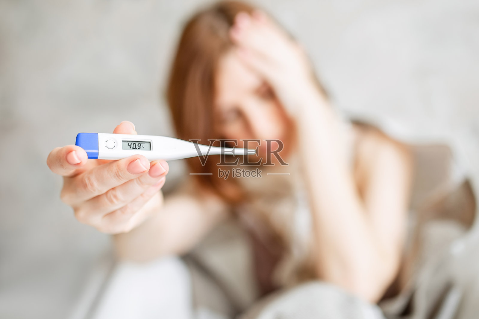 一个生病的年轻女子，围着围巾坐在床上，喉咙痛。喝热茶。一个裹着毯子发烧的女人。照片摄影图片