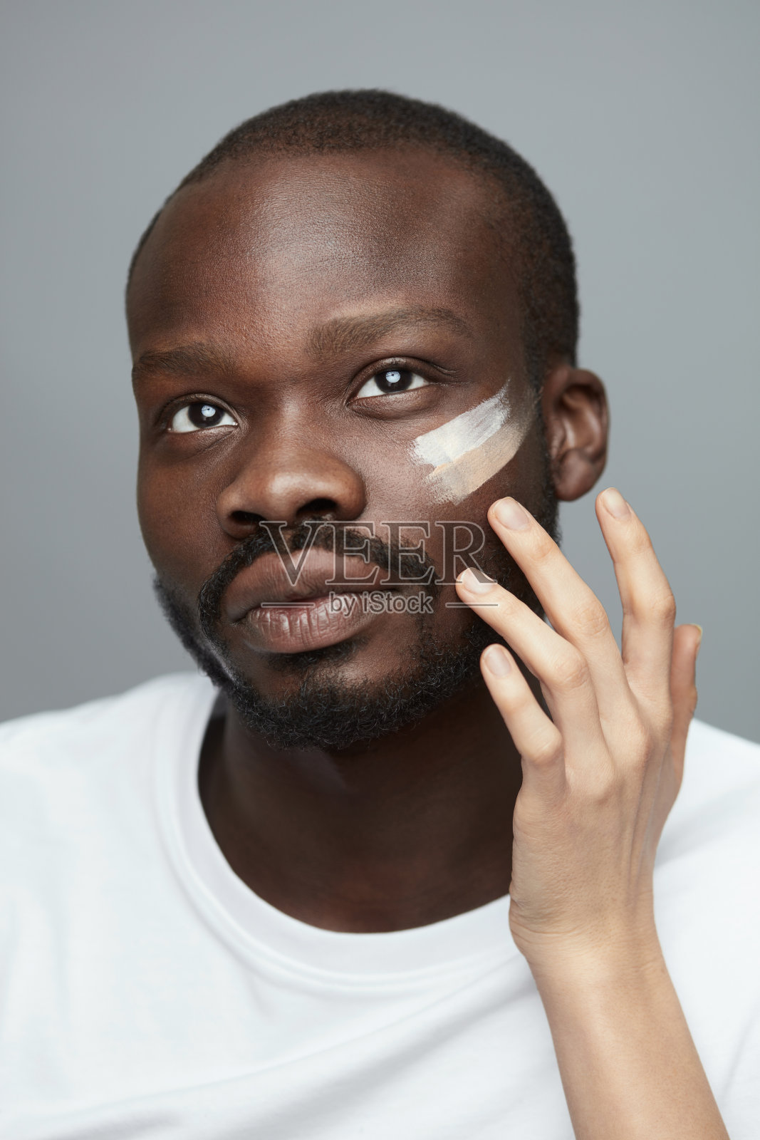 男性化妆。面部治疗程序的男人。女性手给男性脸上涂粉底。美容习惯。照片摄影图片