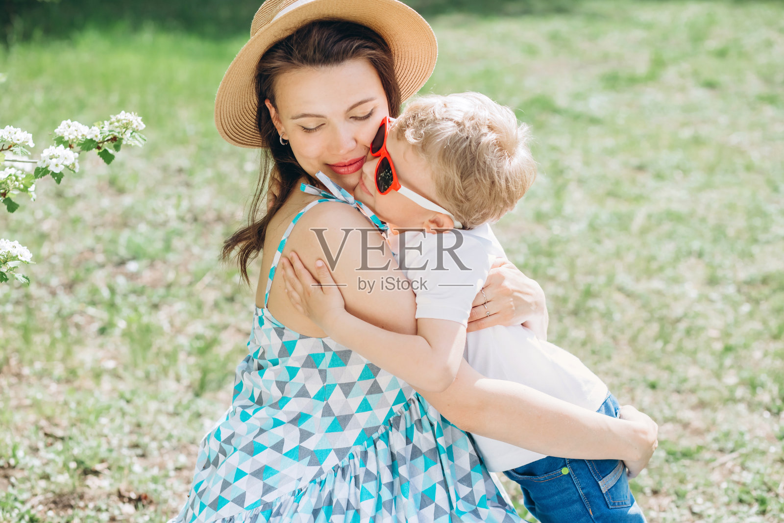 一位年轻的母亲带着一个小儿子坐在公园的草地上。家庭度假。一个年幼的儿子拥抱他的母亲。一个怀孕的女孩带着一个孩子在花园里散步。照片摄影图片