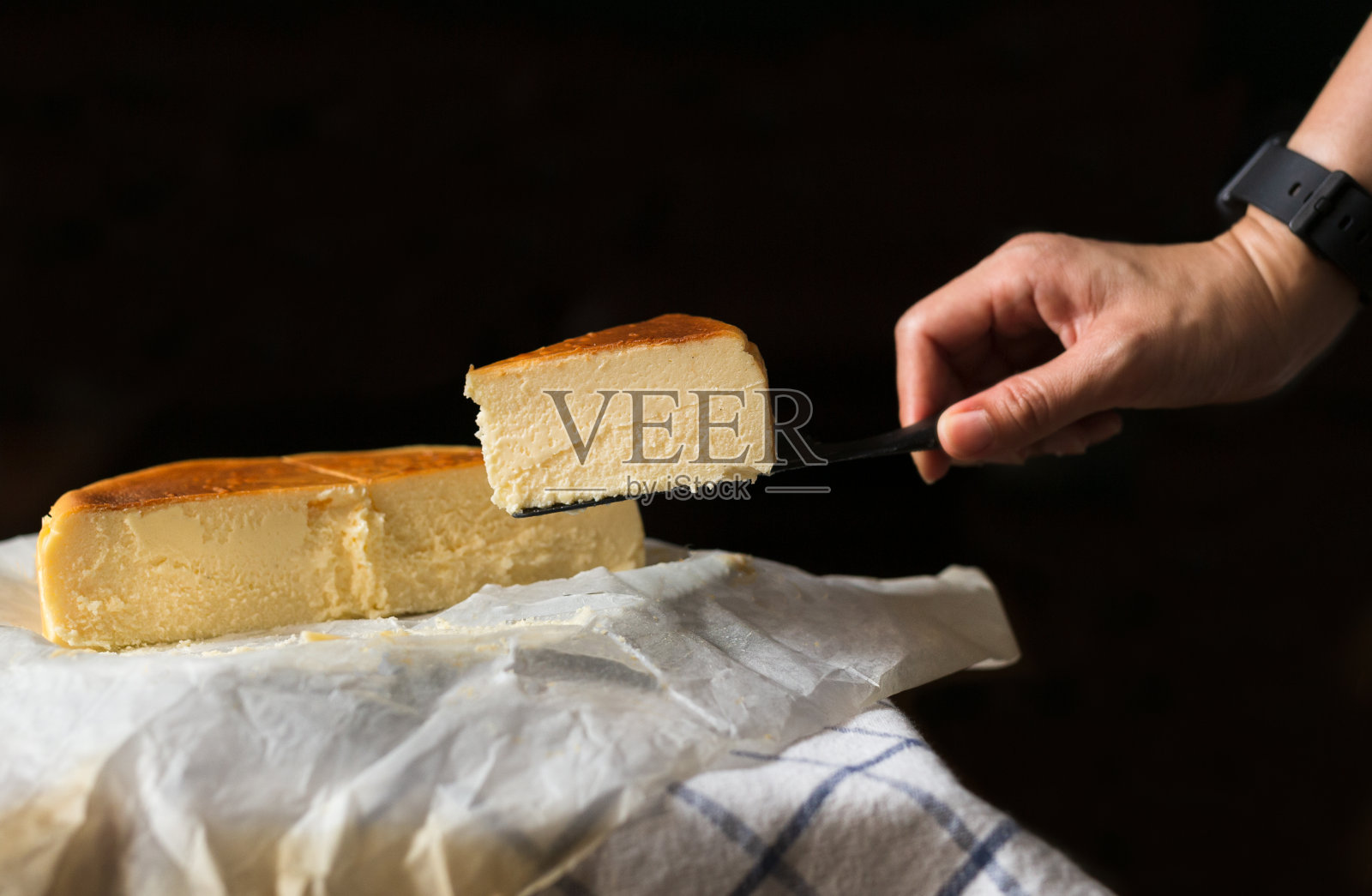 手握一片巴斯克烧焦奶酪蛋糕孤立在黑色背景。照片摄影图片