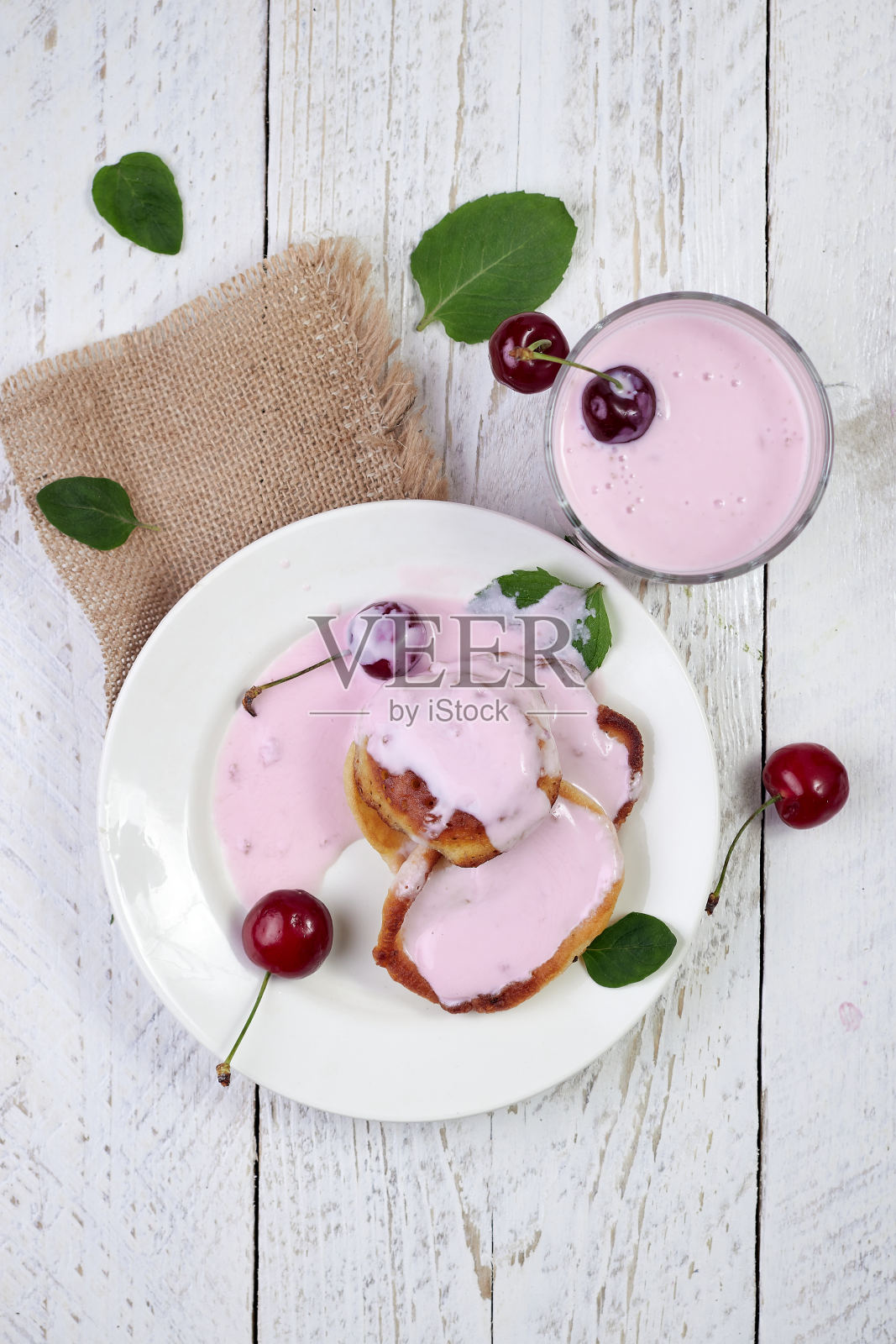 美味美丽的薄饼在一个白色的盘子里，樱桃和酸奶在一个玻璃杯里，在一个轻木制的背景薄荷叶。照片摄影图片