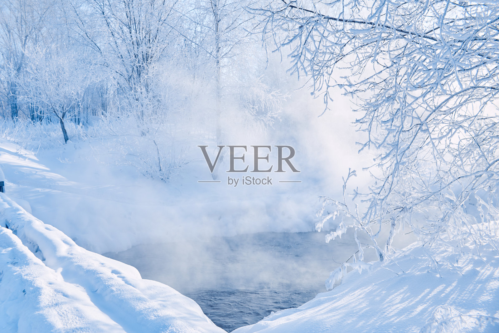 冬天霜冻的早晨河边，雾霾自水。寒冷冬日的阳光。灌木丛和树木在雪地里照片摄影图片