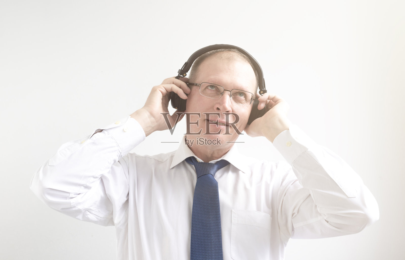 商人戴着耳机听音乐。一名成年男子，身穿白色衬衫，系着蓝色领带，翻白眼，戴着耳机。压力商人的放松和快乐照片摄影图片