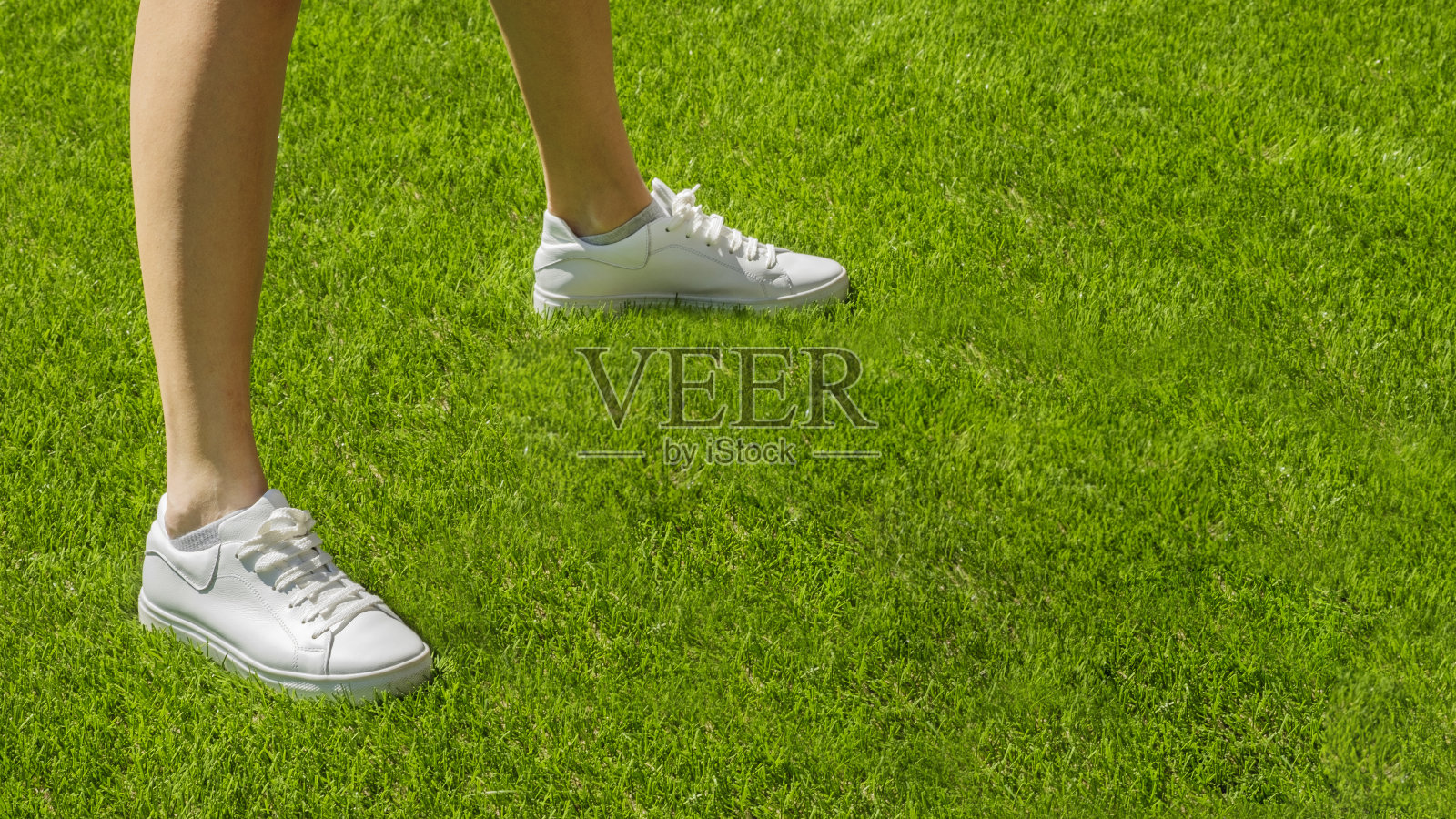 女腿在一个绿色的运动场上白色运动鞋的背景。运动概念，白色运动鞋在草地上跑步。穿着专业运动鞋的腿。在新鲜空气中运动和健身照片摄影图片