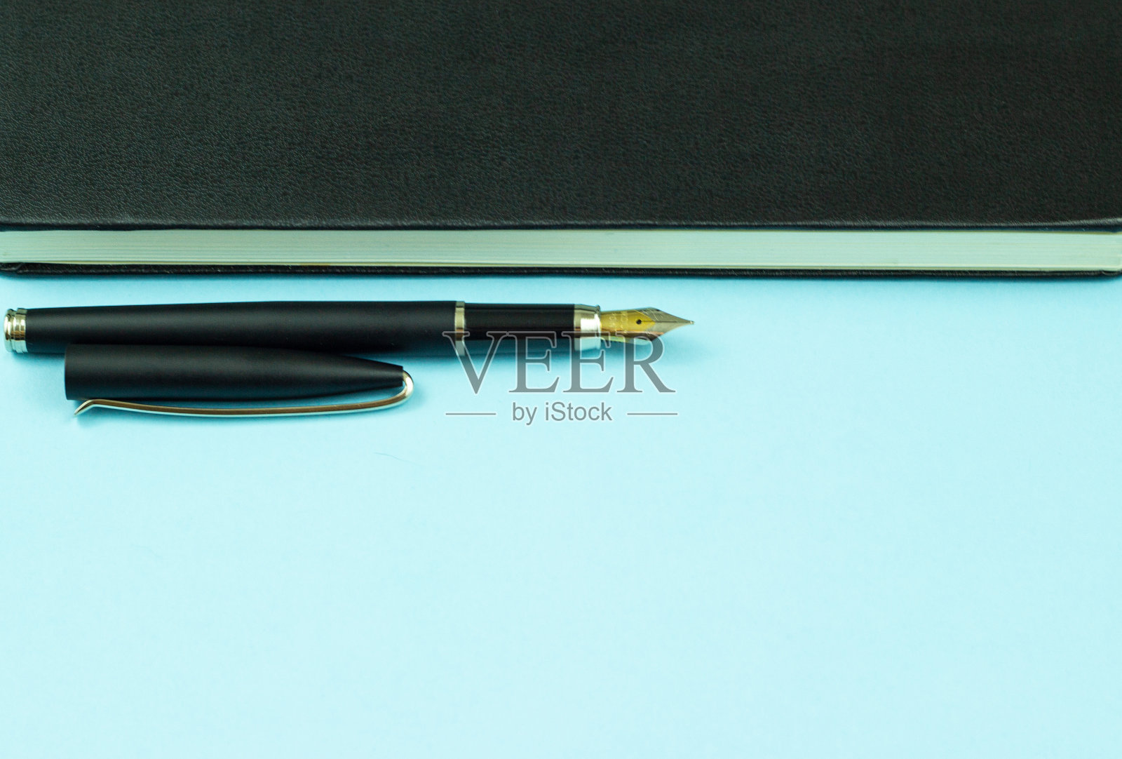 一个带钢笔的黑色笔记本被孤立在蓝色的背景上。照片摄影图片