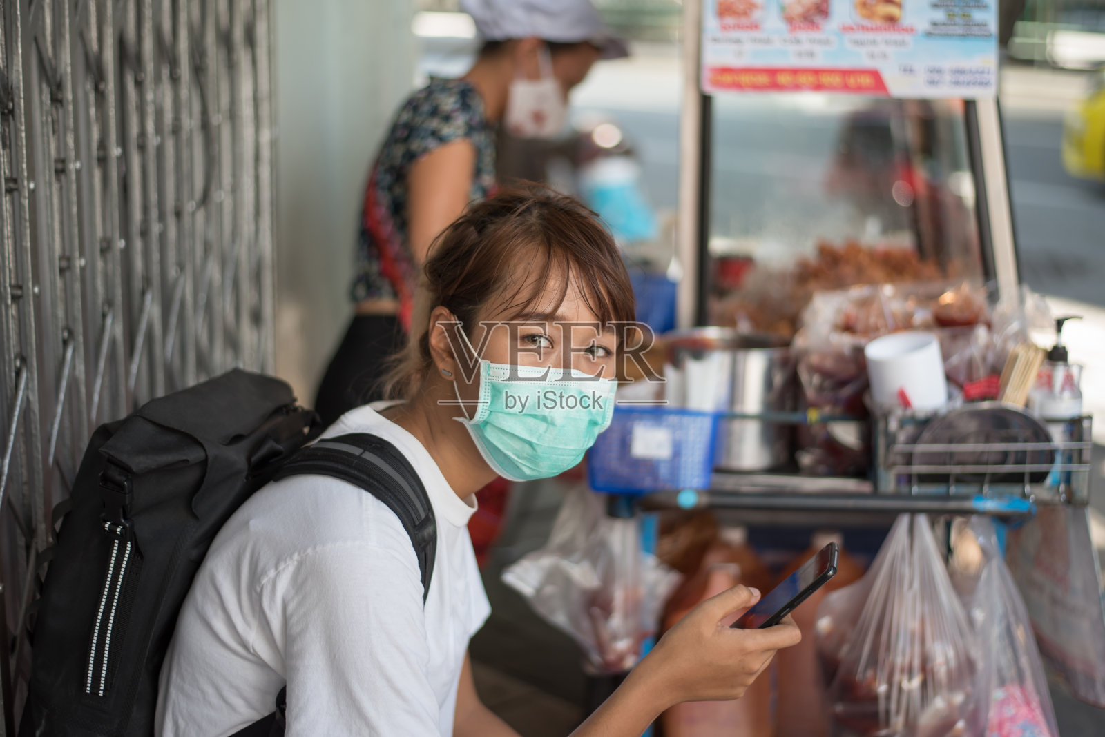亚洲妇女戴着外科口罩，背着背包，前往城市等待街头食品，社交距离，冠状病毒，新冠肺炎照片摄影图片