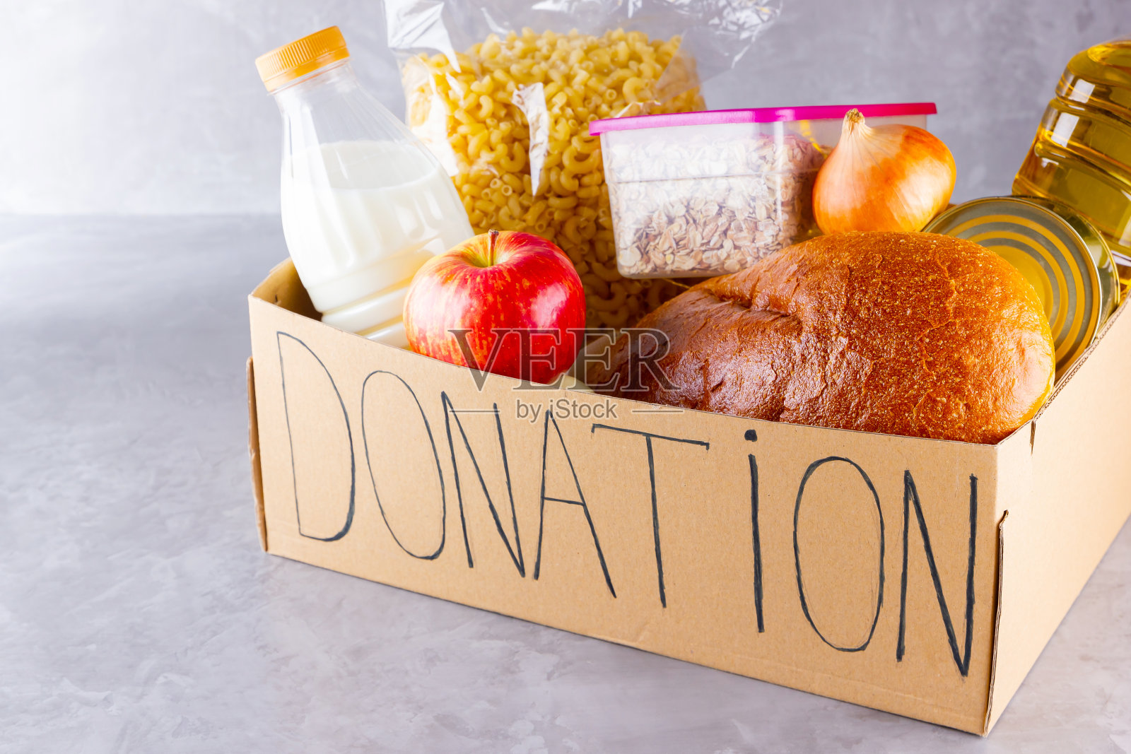 装食物的捐款箱。打开装有油、牛奶、罐头食品、意大利面和面包的纸箱。杂货店设置在灰色背景。捐赠的概念照片摄影图片