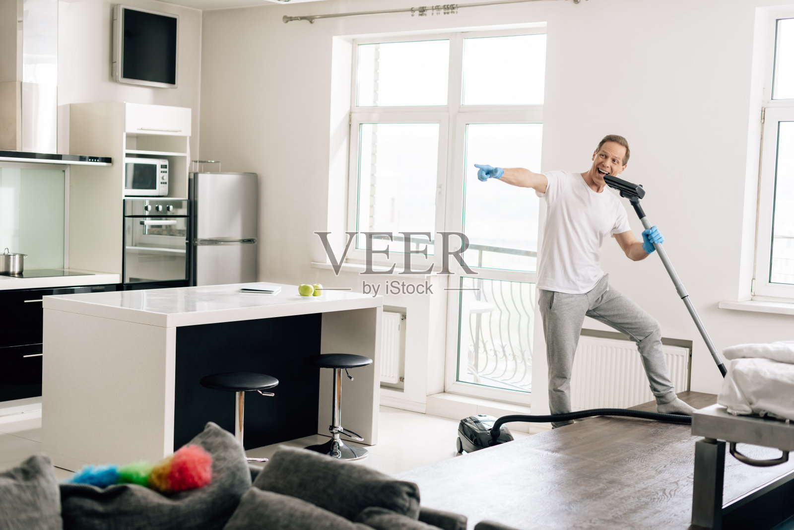 快乐的男人有选择地拿着吸尘器一边唱歌一边用手指指着照片摄影图片