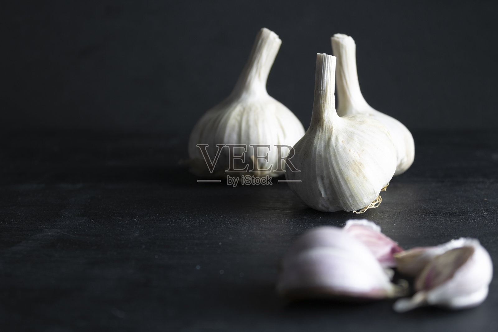 黑色背景上的蒜瓣和未聚焦的蒜头。黑色食品照片摄影图片