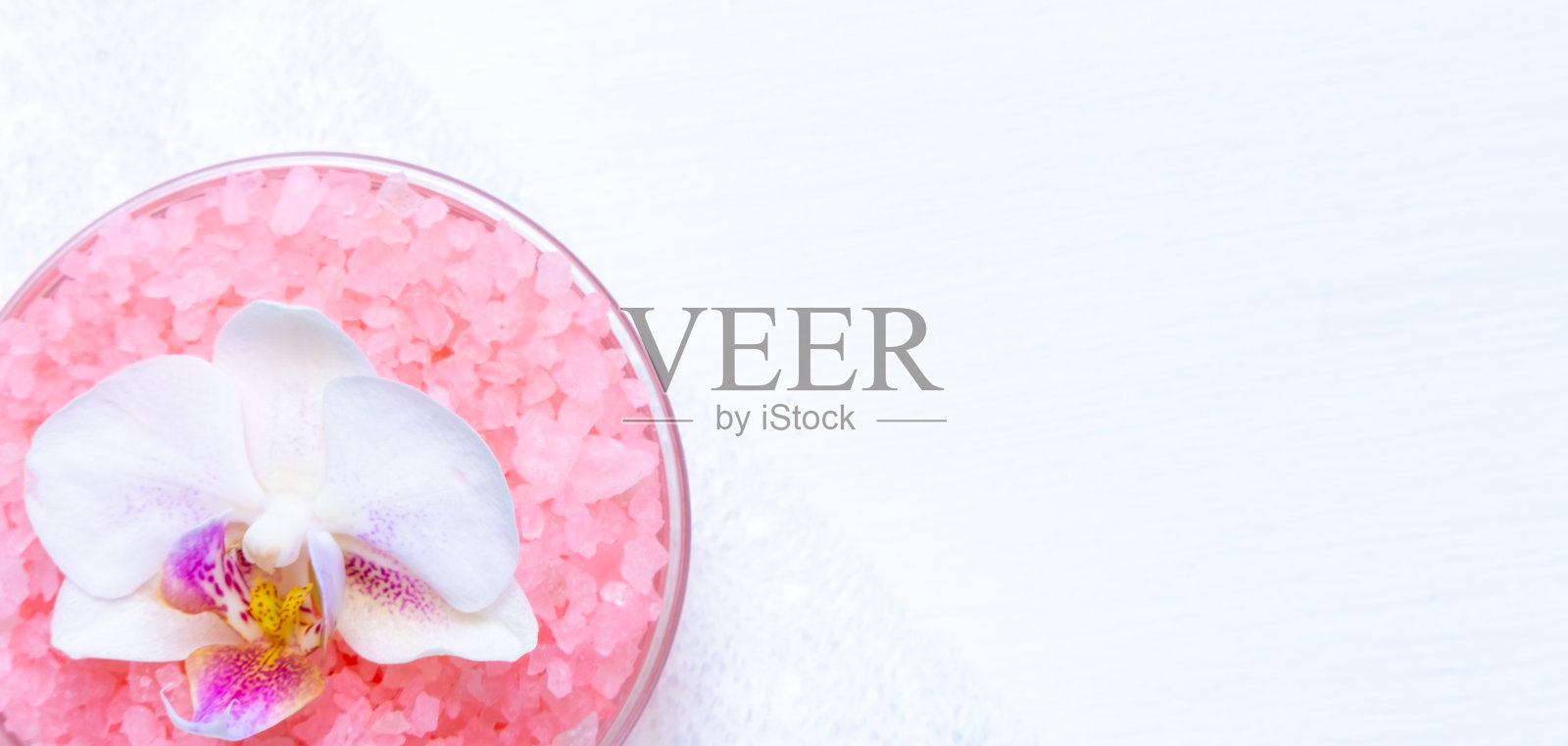 水疗美容理念。粉色的温泉海盐，白色的毛巾和紫色的兰花在白色的木质背景。copyspase flatlay照片摄影图片