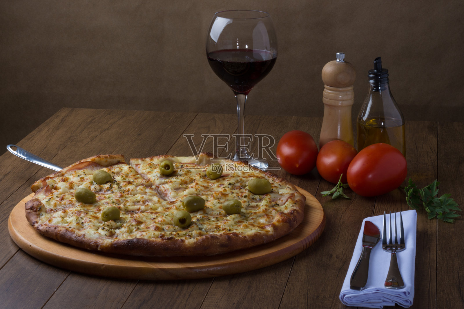 烤沙朗披萨放在木板上。马苏里拉奶酪，加拿大牛腰肉，奶油凝乳和绿橄榄。一片披萨被端上来。摄影水平。照片摄影图片