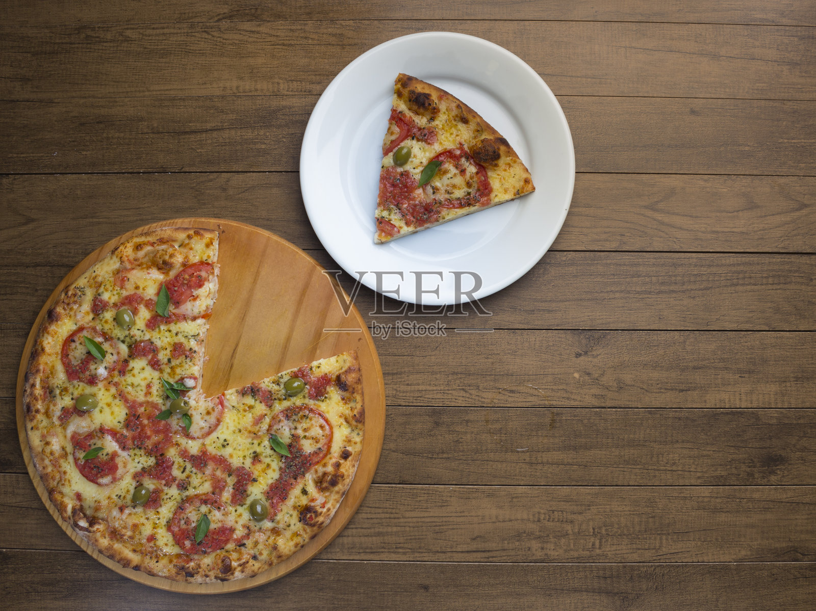 用马苏里拉奶酪、西红柿、罗勒叶和绿橄榄做成的玛格丽特比萨，放在一个白色的盘子里。世界上大多数披萨店的传统食物。前的照片。照片摄影图片