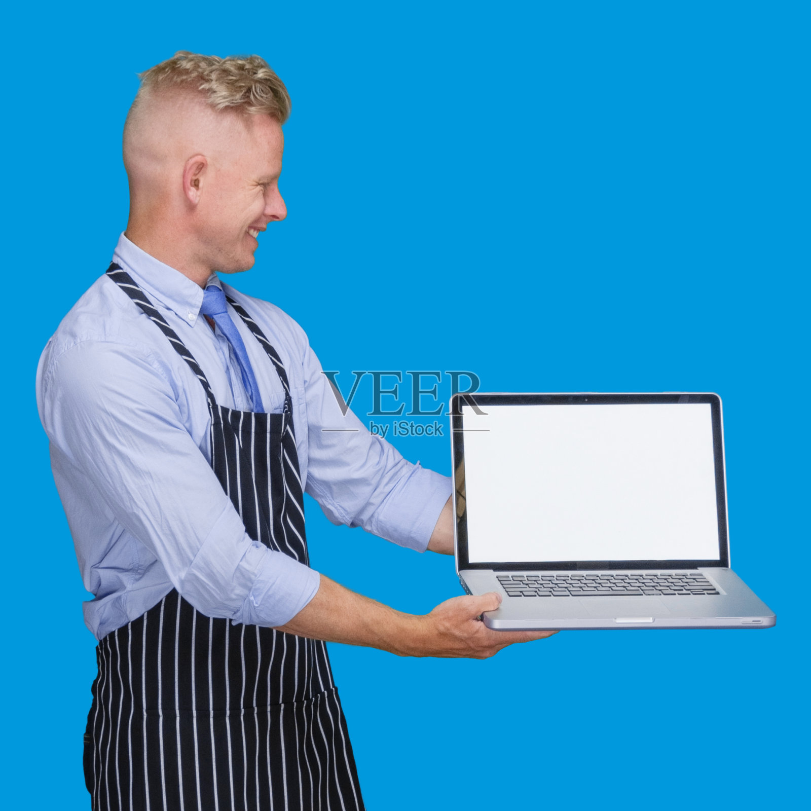 白人年轻男性穿着衬衫站在蓝色背景前使用笔记本电脑照片摄影图片