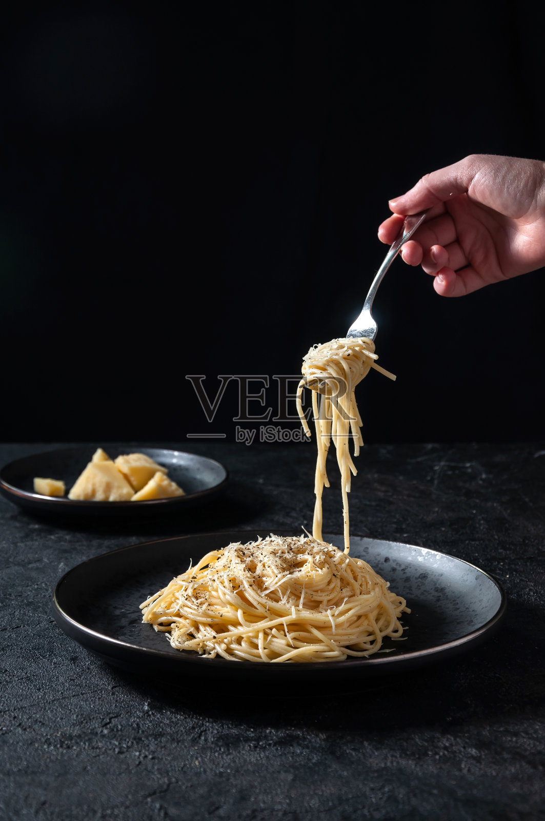 黑胡椒起司意大利面-黑色盘子上的热意大利面，黑色背景上的女人拿着叉子照片摄影图片