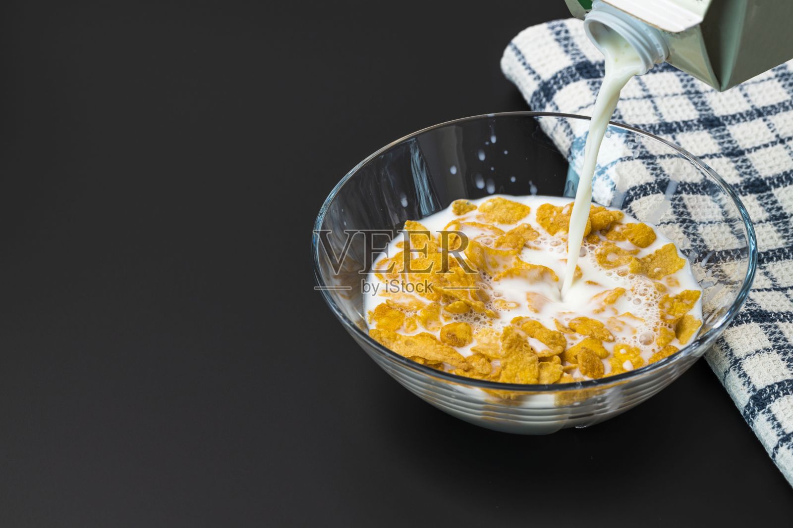 近距离观察牛奶与玉米片倒入玻璃碗的过程。健康饮食的概念。健康食品的背景。照片摄影图片