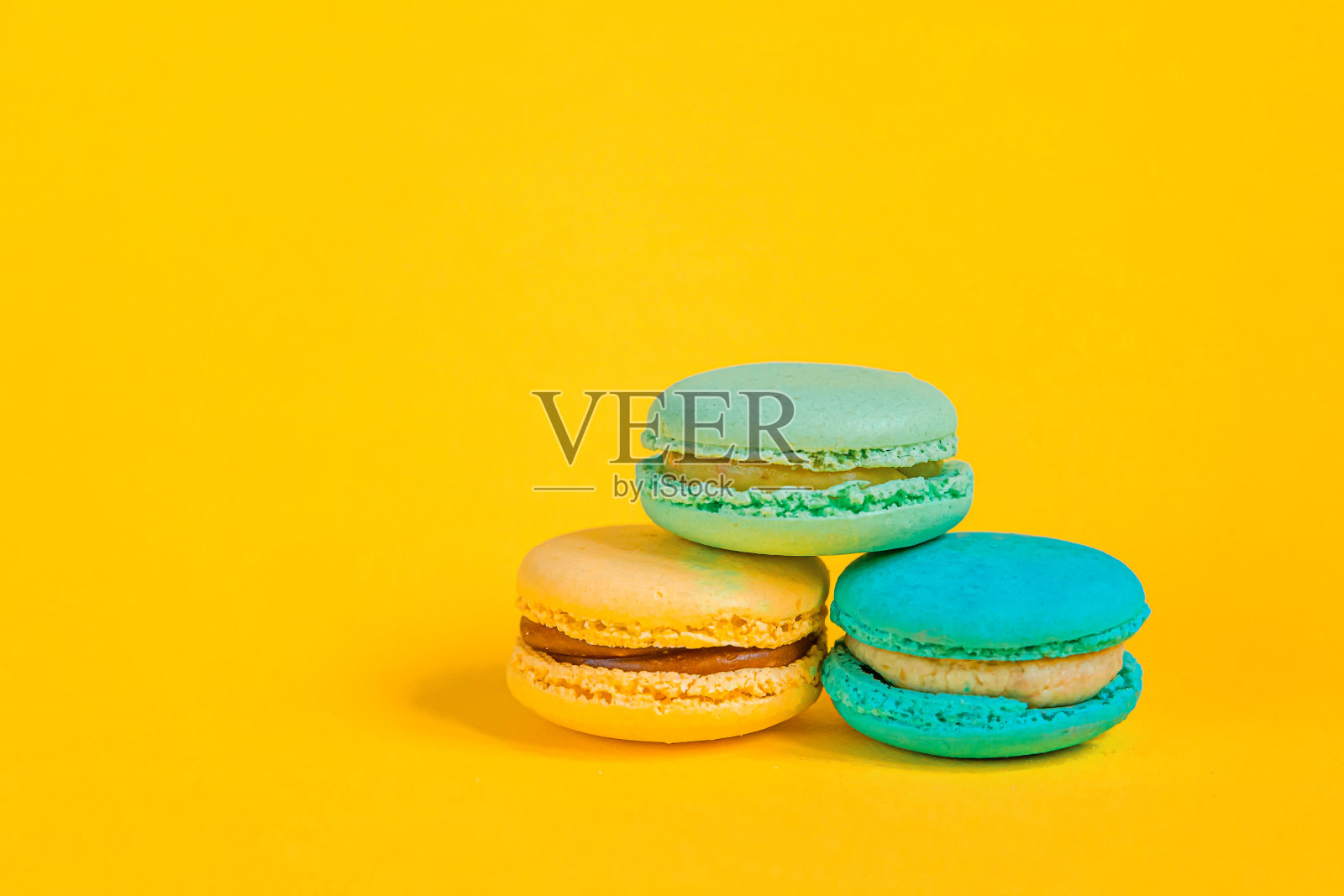 甜杏仁、彩色独角兽、粉色、蓝色、黄色、绿色的马卡龙或马卡龙甜品蛋糕孤立在时髦的黄色、现代的时尚背景上。法国甜的饼干。最小的食品烘焙概念拷贝空间照片摄影图片