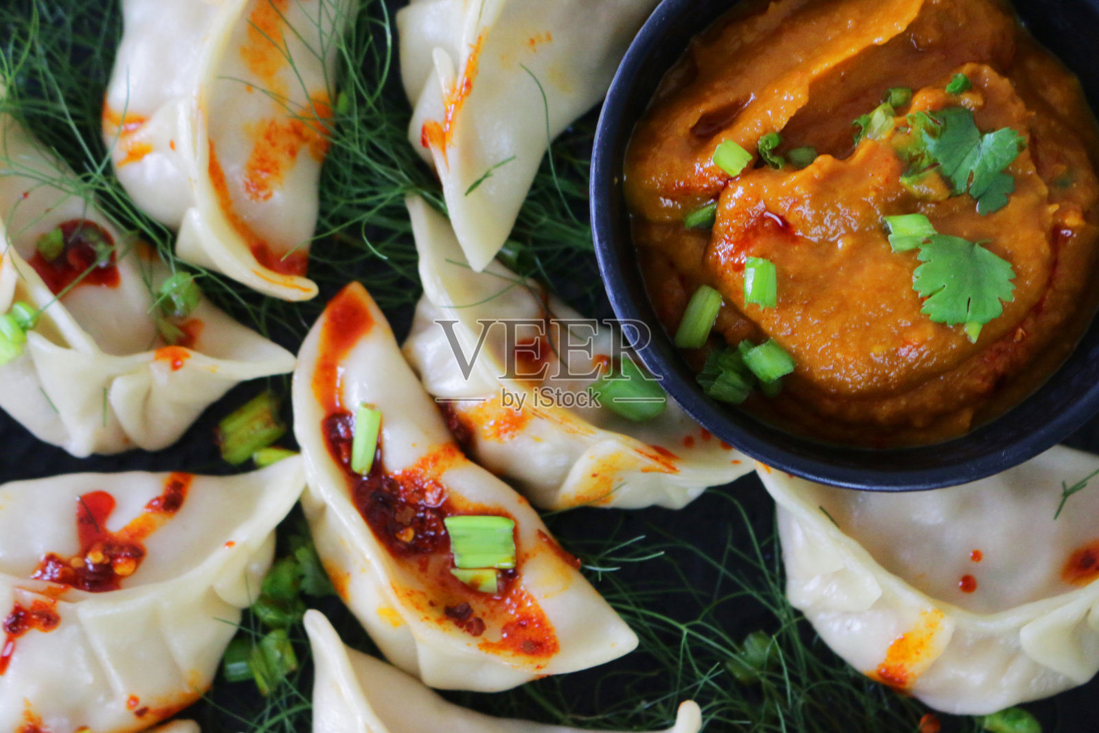 蒸饺(南亚饺子)，白面粉和水面团，充满鸡肉和杂烩蔬菜，淋上辣椒油，放在盘子里，周围是用橙色辣酱蘸酱的小模子，俯瞰美景照片摄影图片