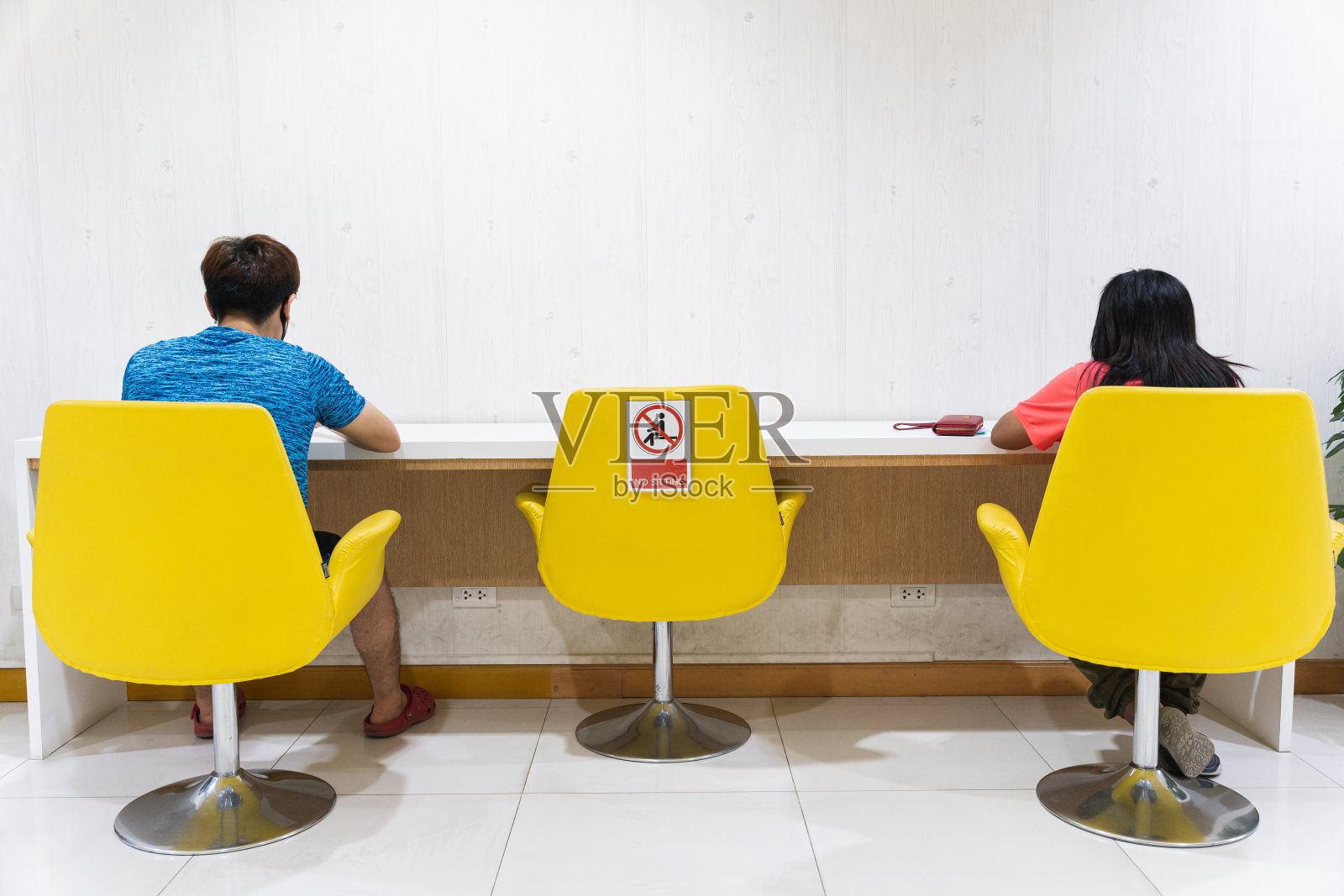 为了保护和预防新冠肺炎，公共椅子上的年轻男女都被限制坐着。社会距离的概念。照片摄影图片