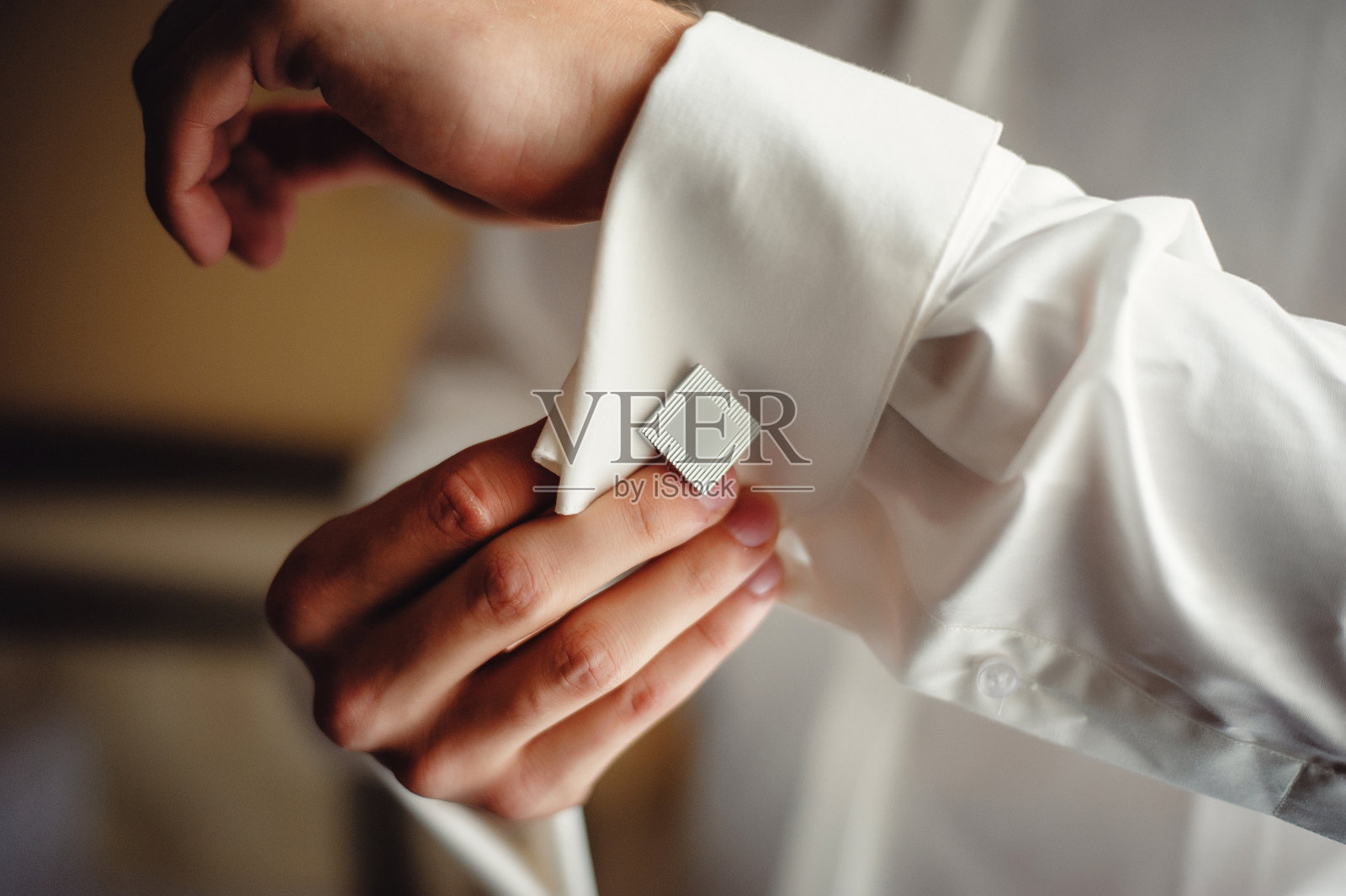 一个成功的人在白衬衫的袖口上戴着银色的袖扣。新郎的手把袖扣扣在白衬衫的袖子上。特写男人的配件。新郎的早晨照片摄影图片