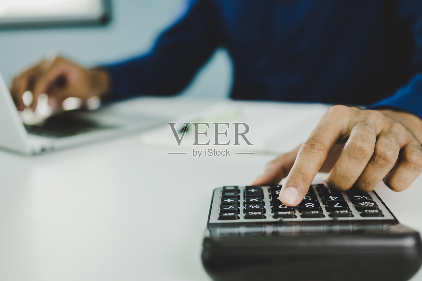 蓝色衬衫的商人用计算器计算财务，在笔记本电脑上工作，在家里的办公桌上报告，数字营销，企业财务，会计概念照片摄影图片