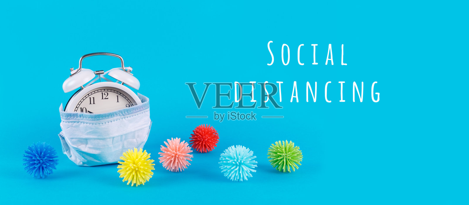 闹钟在医疗面具和塑料球作为病毒在蓝色与社会距离的措辞。流行病、社会隔离、冠状病毒新冠病毒概念照片摄影图片