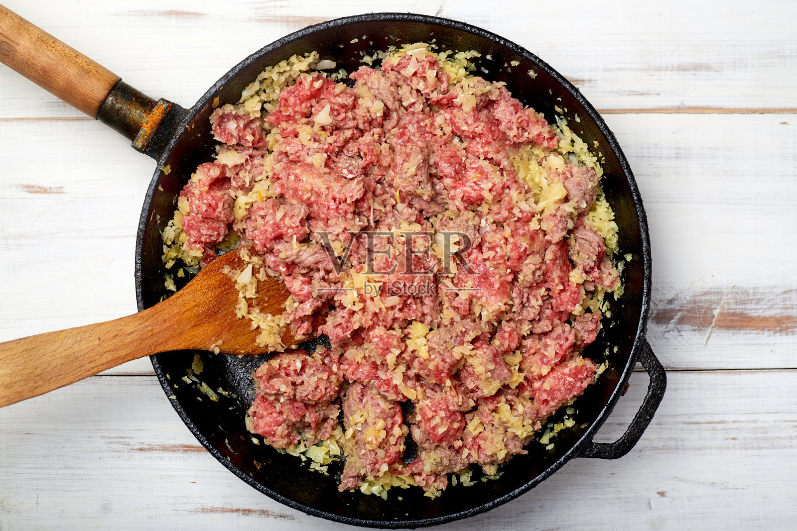 在平底锅里放入碎肉和洋葱，背景是浅色的木头。烹饪配料。照片摄影图片