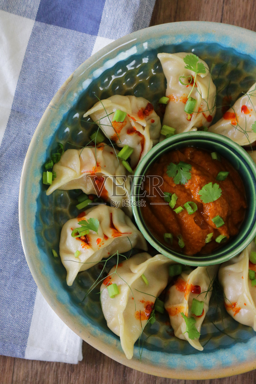 蒸饺(南亚饺子)，白面粉和水面团，充满鸡肉和杂烩蔬菜，淋上辣椒油，放在盘子里，周围是用橙色辣酱蘸酱的小模子，俯瞰美景照片摄影图片
