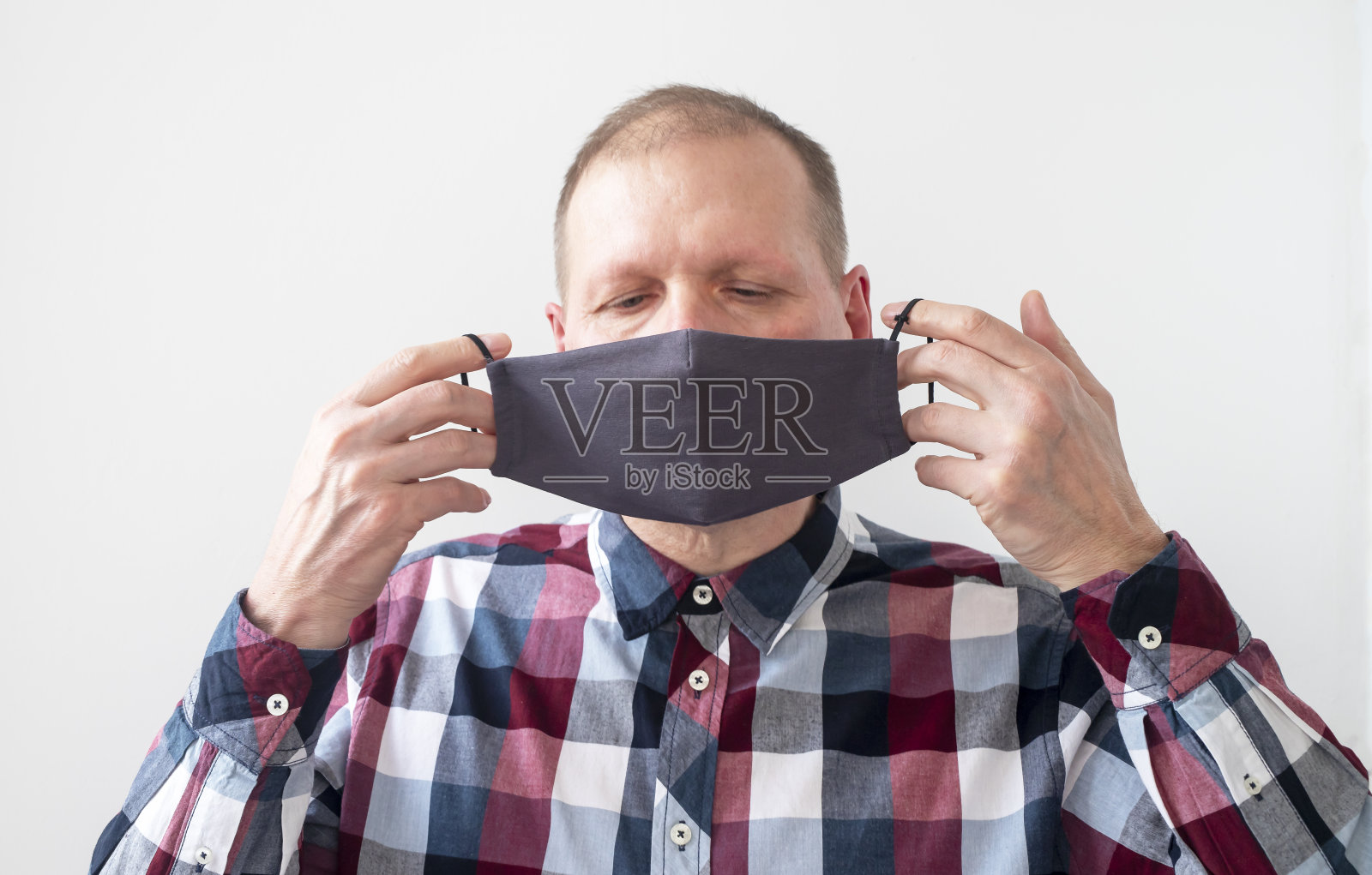 成年男子身穿衬衫，脸上戴着灰色医用口罩，以预防冠状病毒传染病。成年男子戴上防护口罩作为COVID-19预防措施。白色背景。健康的概念照片摄影图片