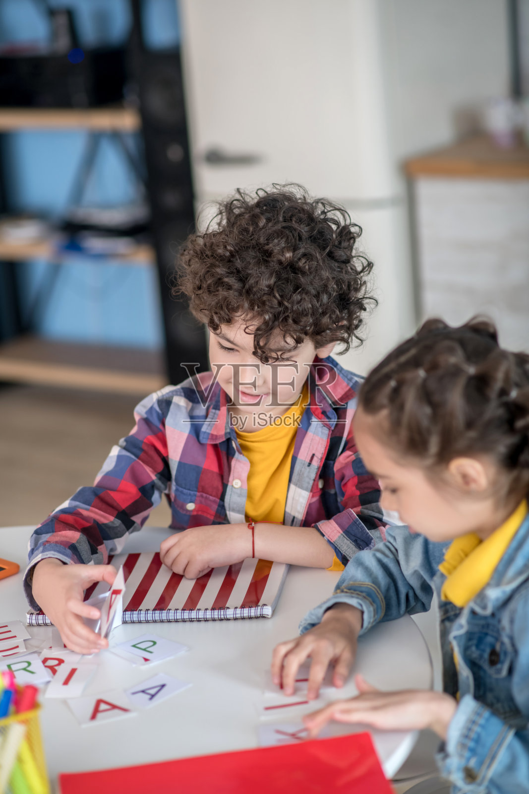 卷发男孩和黑发女孩坐在圆桌旁玩字母照片摄影图片