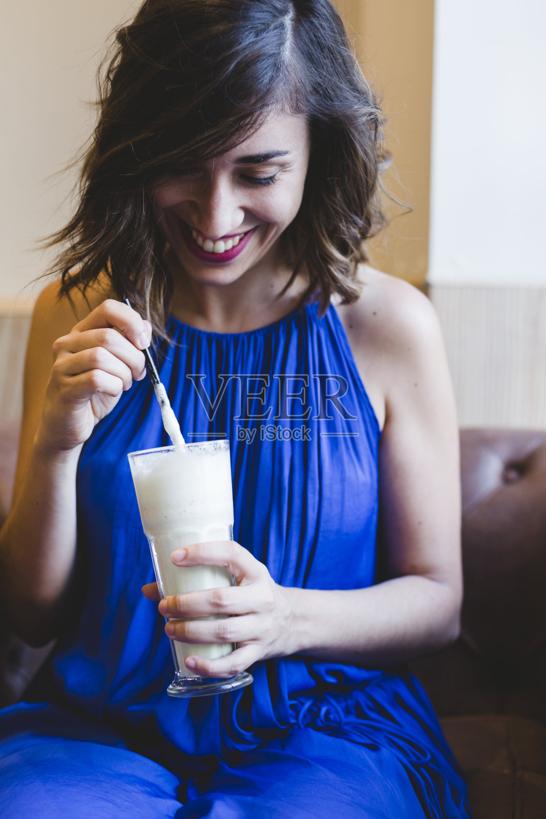 年轻美丽的女人在咖啡馆享受一杯冰沙饮料。休闲的蓝色裙子。现代生活在室内照片摄影图片