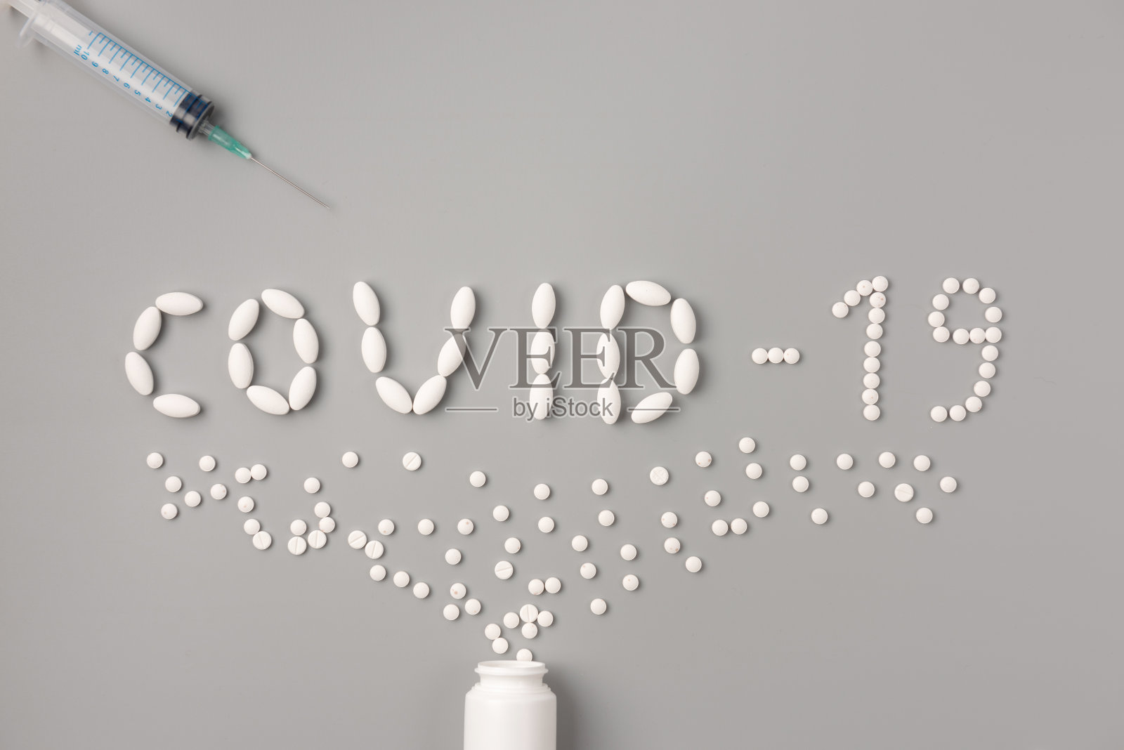 以“covid -19”字为形状的平铺药片，灰色背景上有注射器和药丸，这是一种保健理念，旨在防止covid -19大流行的传播照片摄影图片
