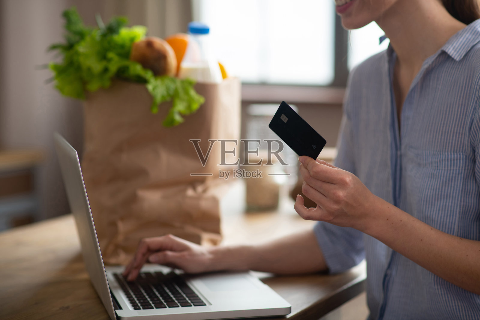 穿着灰色家装的女孩拿着信用卡，在网上付款照片摄影图片