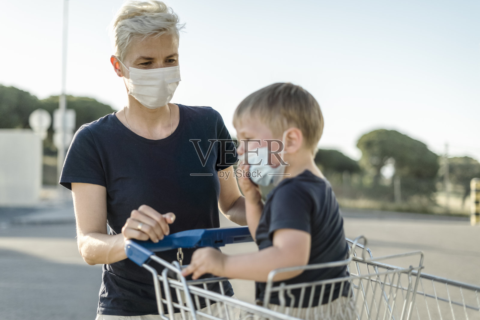 母亲带着小儿子在购物车里戴着防护口罩去超市照片摄影图片
