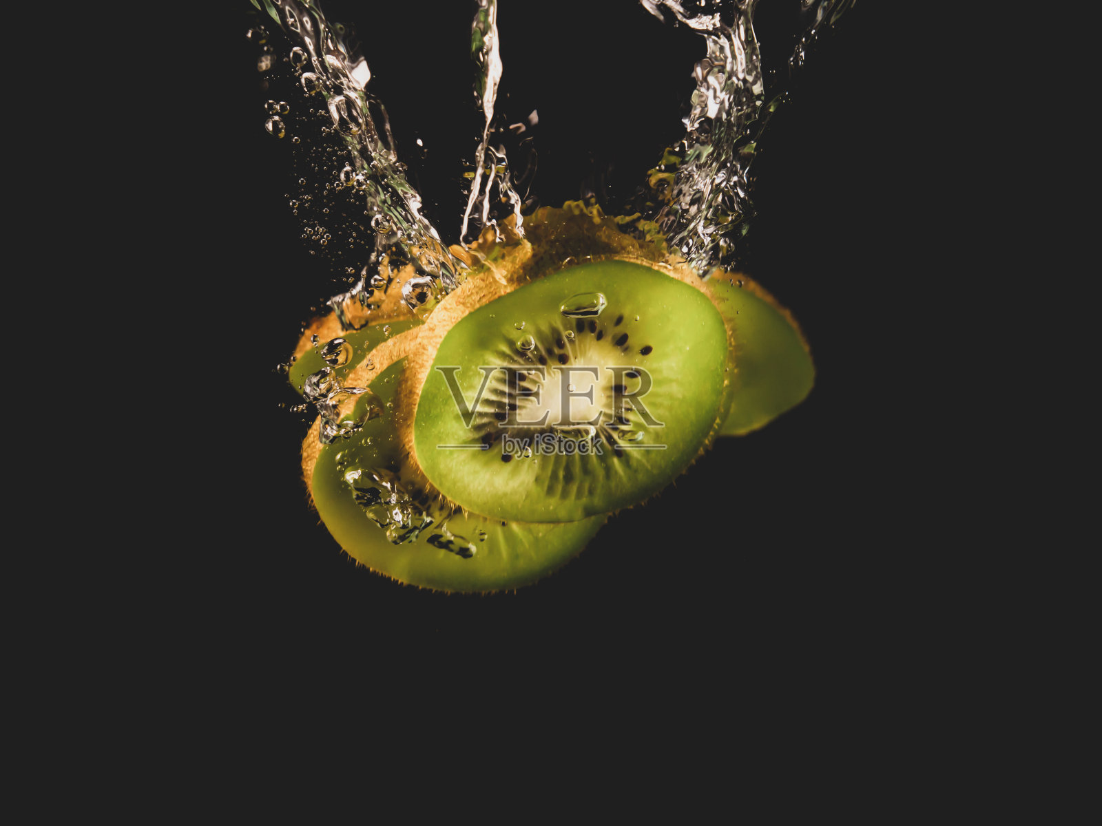 新鲜的猕猴桃片落入清澈的水中，黑色的背景上有很大的飞溅。一群多汁的猕猴桃掉进水中溅起水花。绿色的猕猴桃片落在带有气泡的水中照片摄影图片