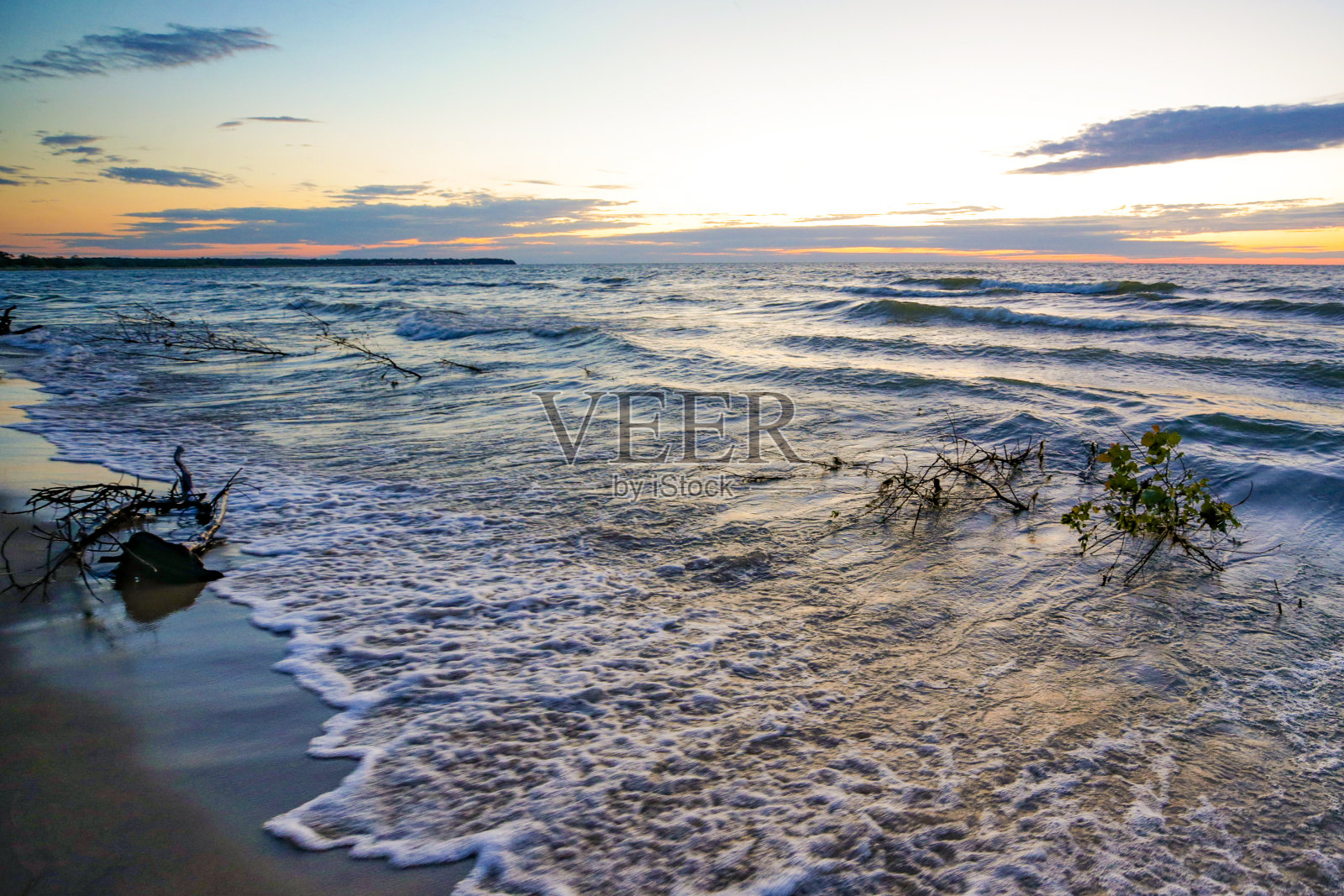 在一个风很大的日子里，日落时海浪拍打着休伦湖上的密歇根海滩照片摄影图片