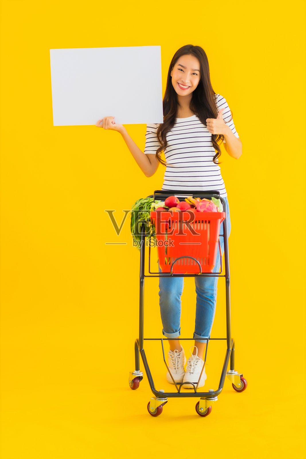 肖像美丽的年轻亚洲女人与杂货篮子购物车和显示白色空板照片摄影图片