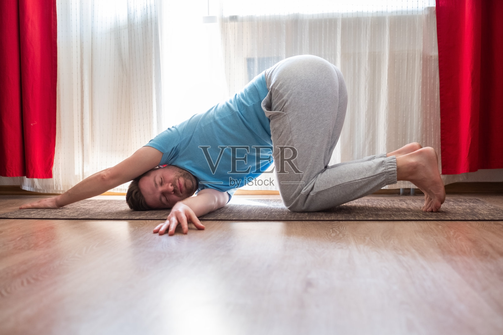 一个年轻人在地板上做扭曲体式，在他的客厅里伸展照片摄影图片