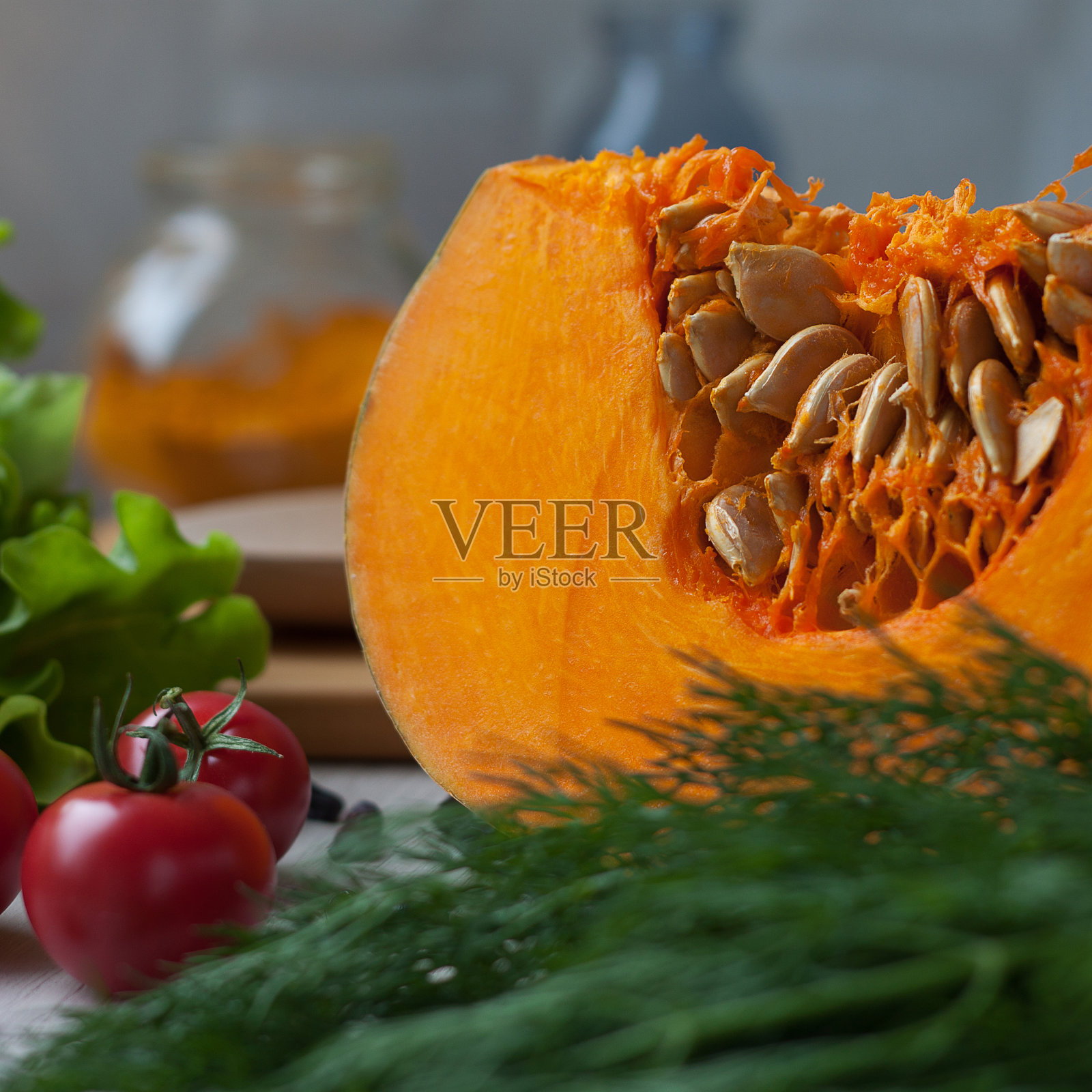 桌上放着圣女果，一块生的新鲜南瓜，还有种子和绿色蔬菜照片摄影图片