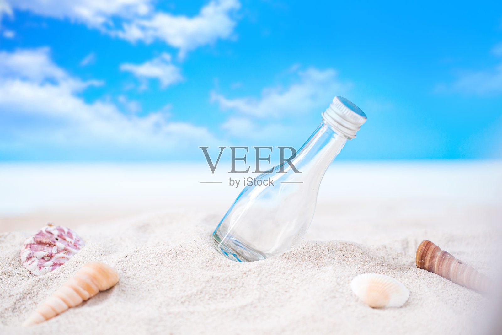 瓶子在沙滩上和贝壳在模糊的热带蓝色的海洋和清澈的蓝色天空照片摄影图片