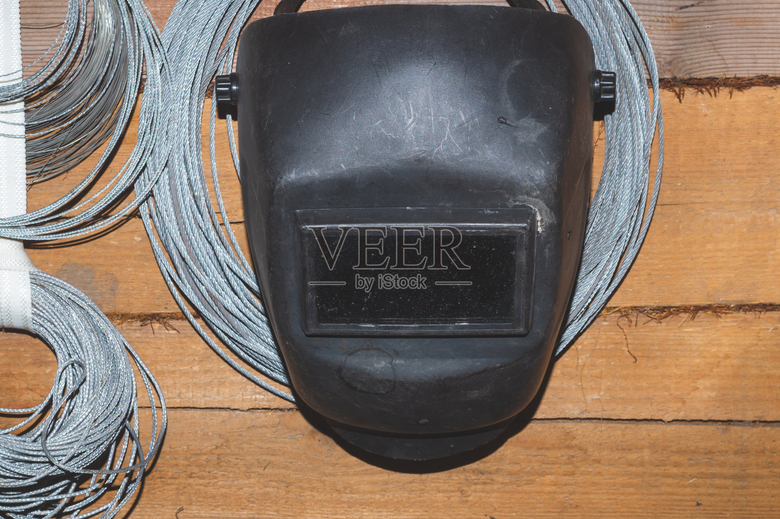 挂在木墙上的焊接面罩。钢丝绳的绞丝。头盔的铁匠照片摄影图片